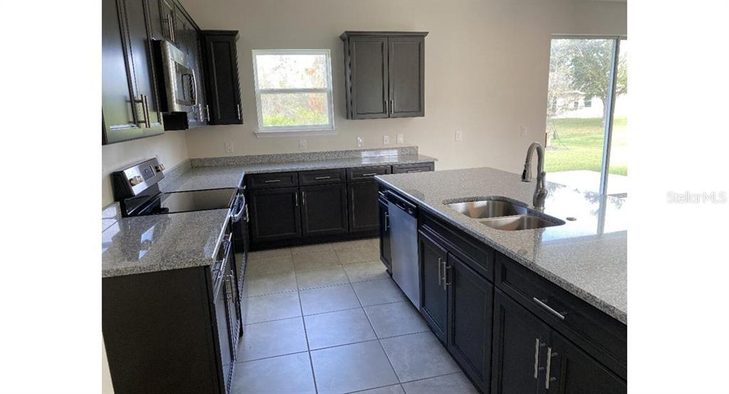 A kitchen features dark cabinets, granite countertops, stainless steel appliances, and tile flooring — 7050 BECKWITH AVENUE, NORTH PORT, FL