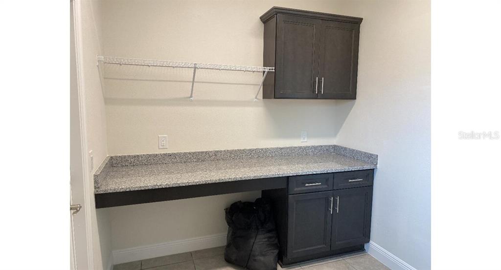 A laundry room features dark cabinets, a granite countertop, and a white wire shelf — 7050 BECKWITH AVENUE, NORTH PORT, FL