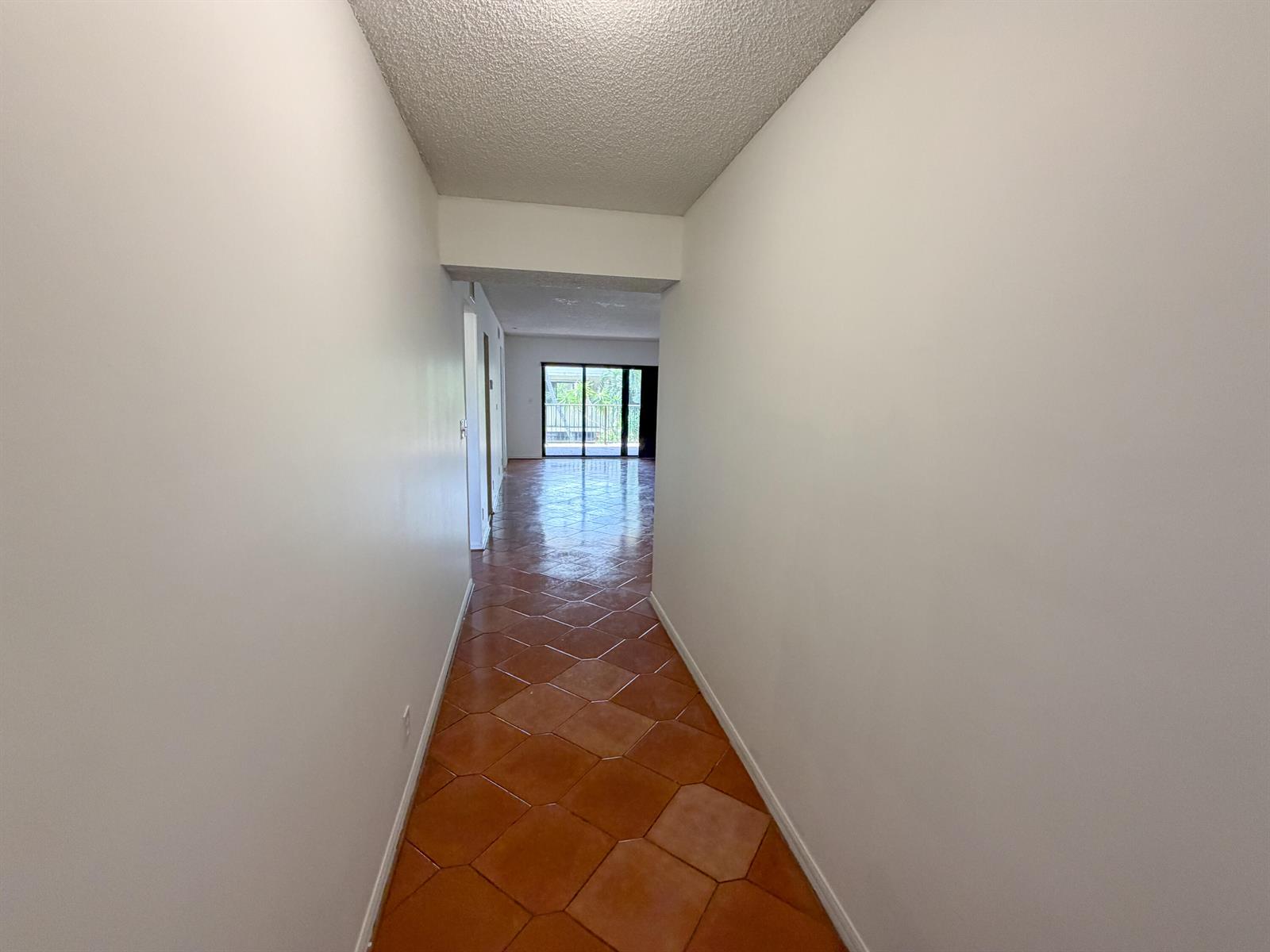 A hallway with terracotta tile flooring leads toward a living area with sliding glass doors — 241 SE 11th Avenue # 241a, Pompano Beach FL 33060, POMPANO BEACH, FL