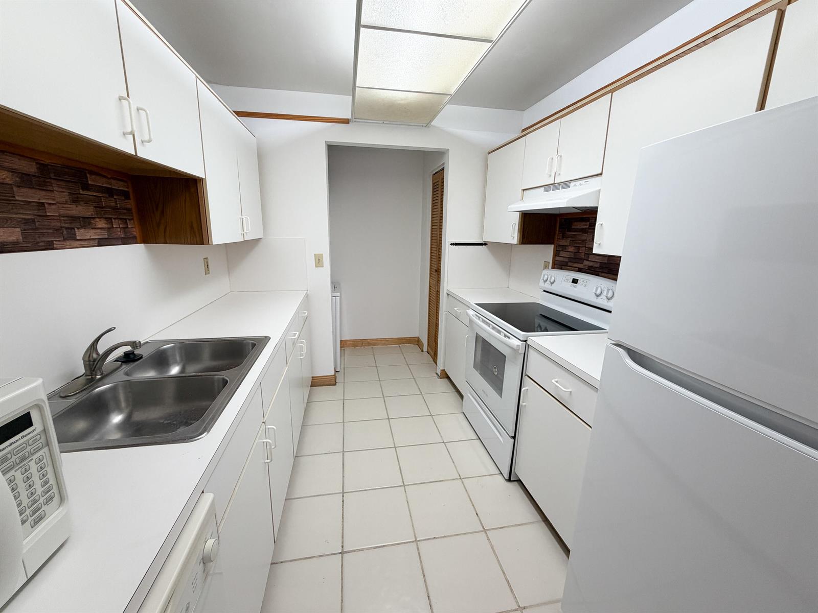 A galley kitchen features white cabinets, white appliances, a double sink, and tiled flooring — 241 SE 11th Avenue # 241a, Pompano Beach FL 33060, POMPANO BEACH, FL