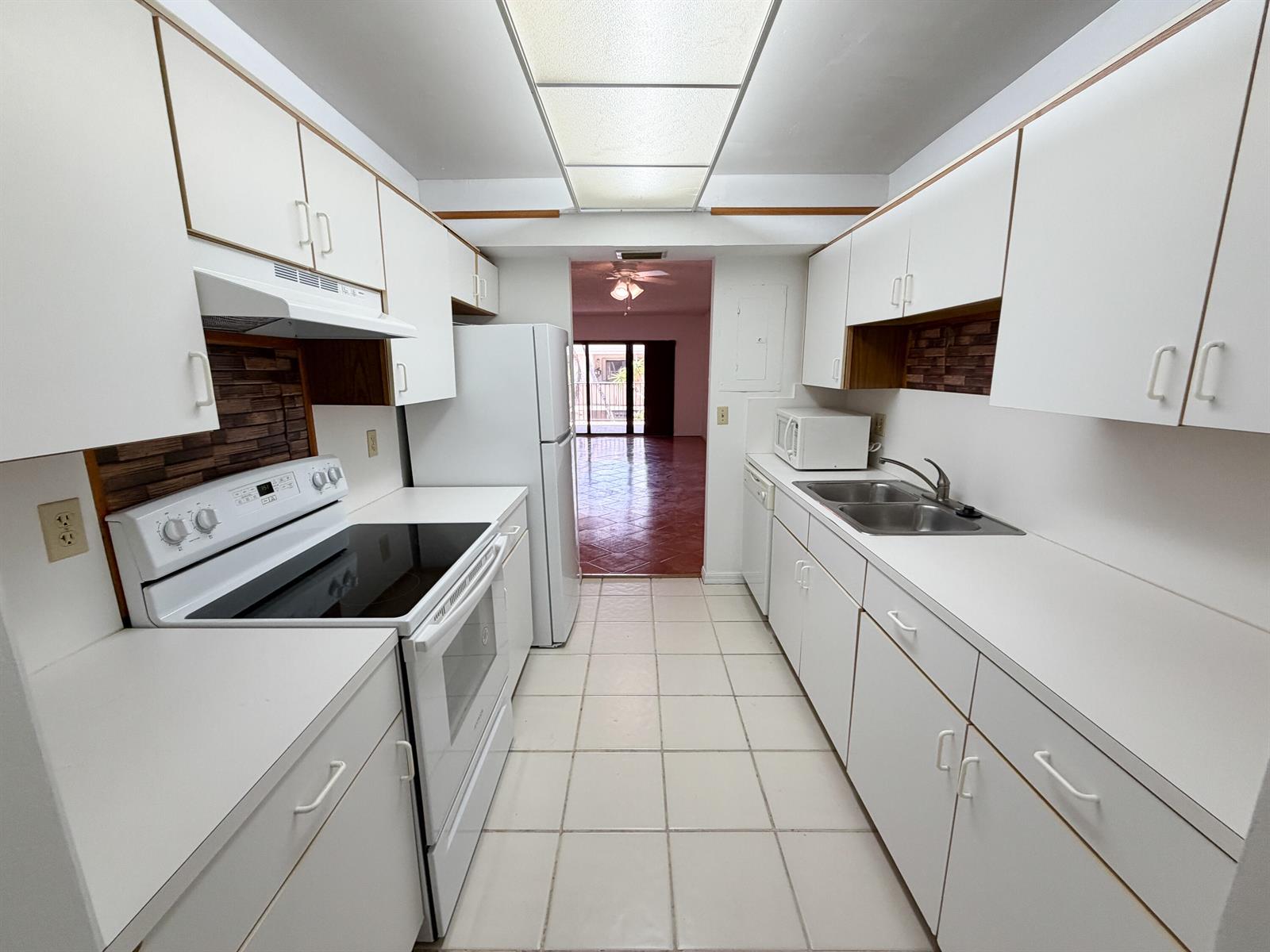 A galley kitchen features white cabinets, white appliances, tiled flooring, and a drop ceiling light — 241 SE 11th Avenue # 241a, Pompano Beach FL 33060, POMPANO BEACH, FL