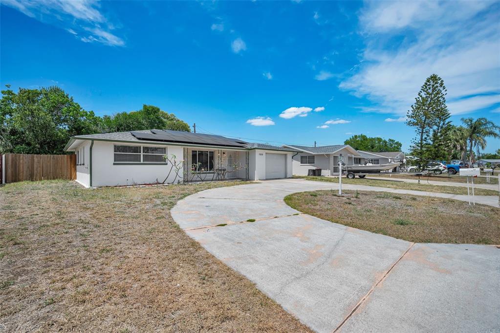 A single-story house with a concrete driveway, solar panels on the roof, and a lawn — 7529 REDCOAT AVENUE, PORT RICHEY, FL