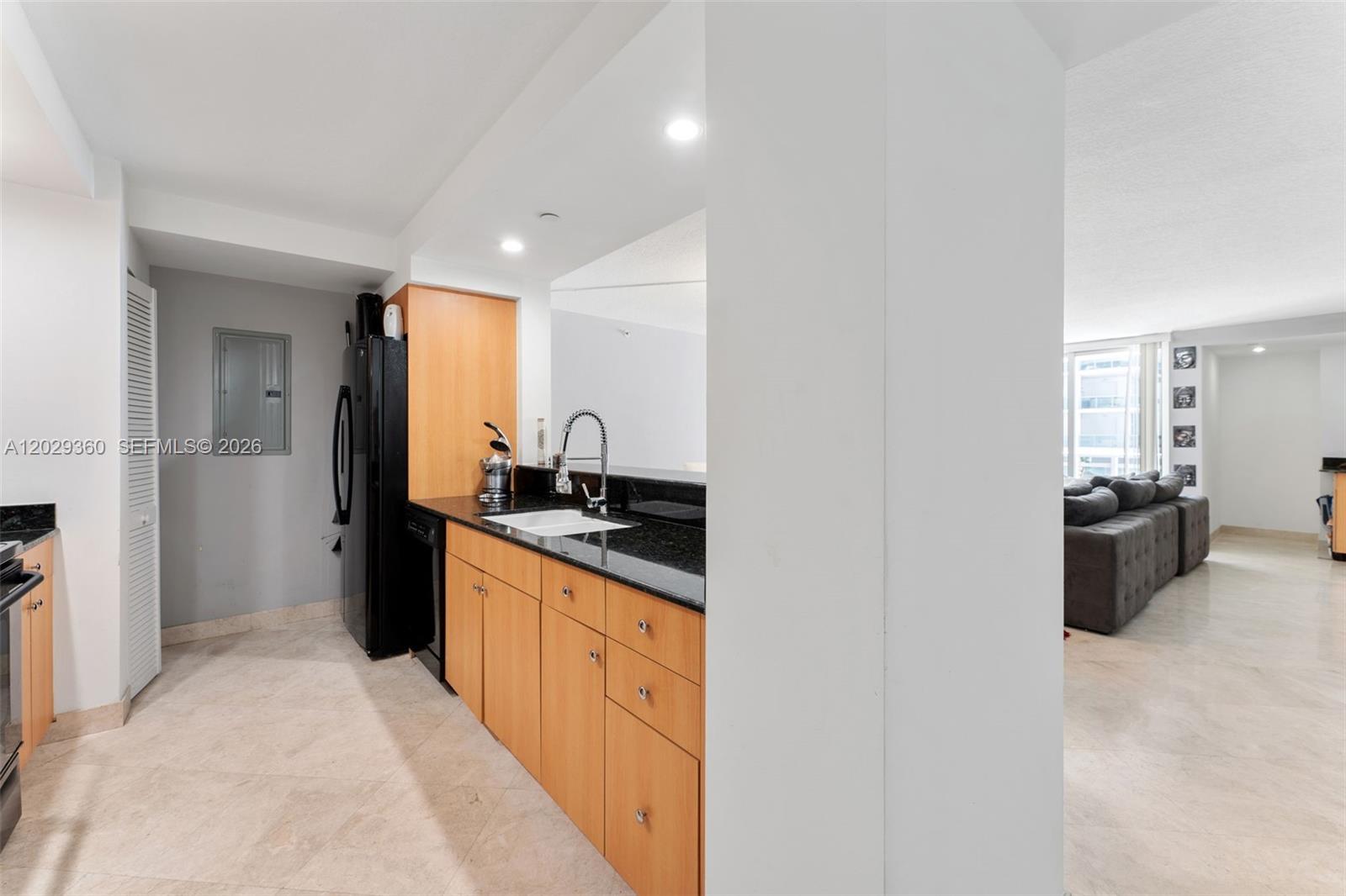 A kitchen with light wood cabinets, black countertops, and a black refrigerator — 6917 Collins Ave # 607, Miami Beach FL 33141, MIAMI BEACH, FL
