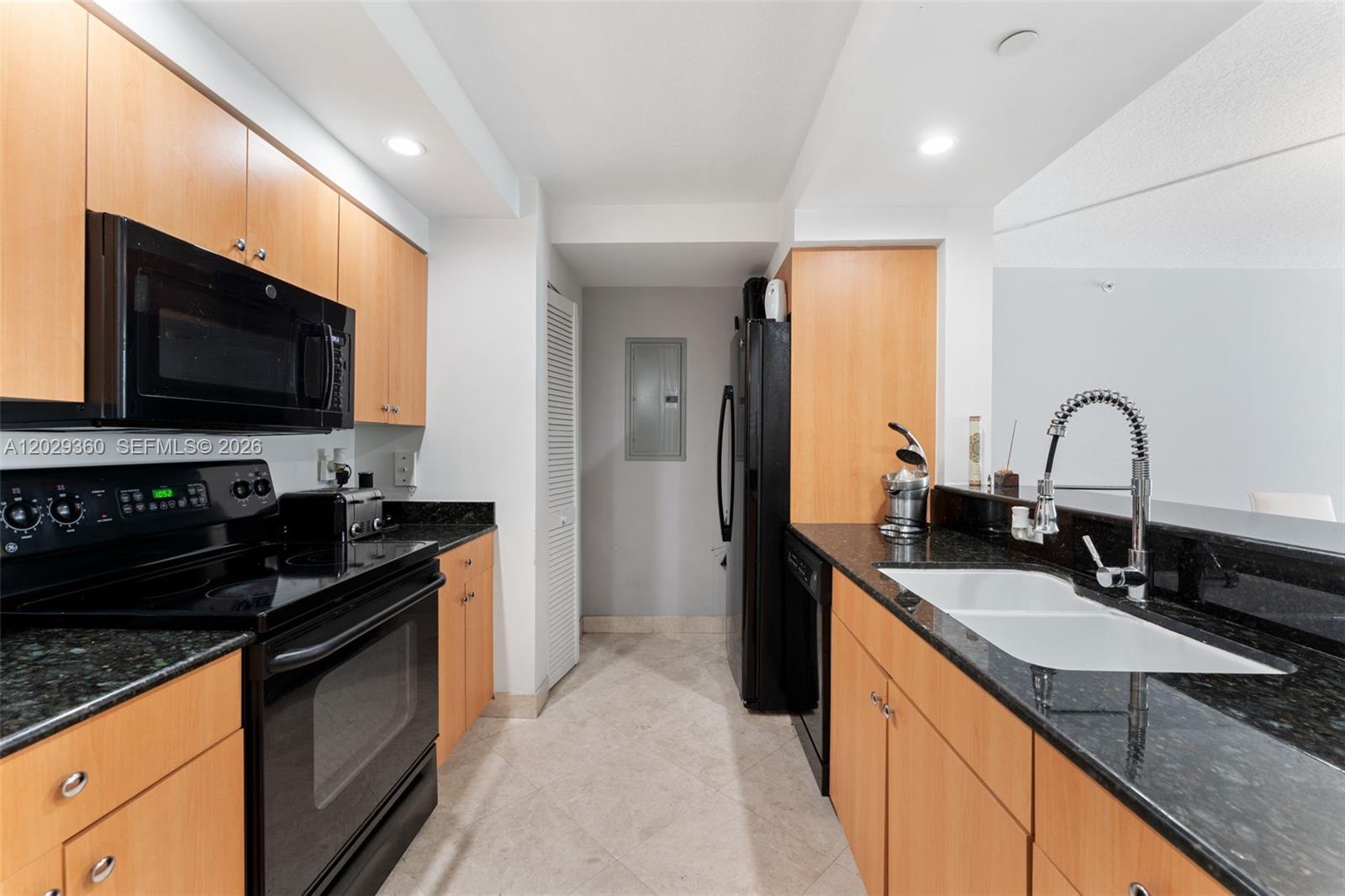 A kitchen features light wood cabinets, black appliances, dark granite countertops, and a double sink — 6917 Collins Ave # 607, Miami Beach FL 33141, MIAMI BEACH, FL