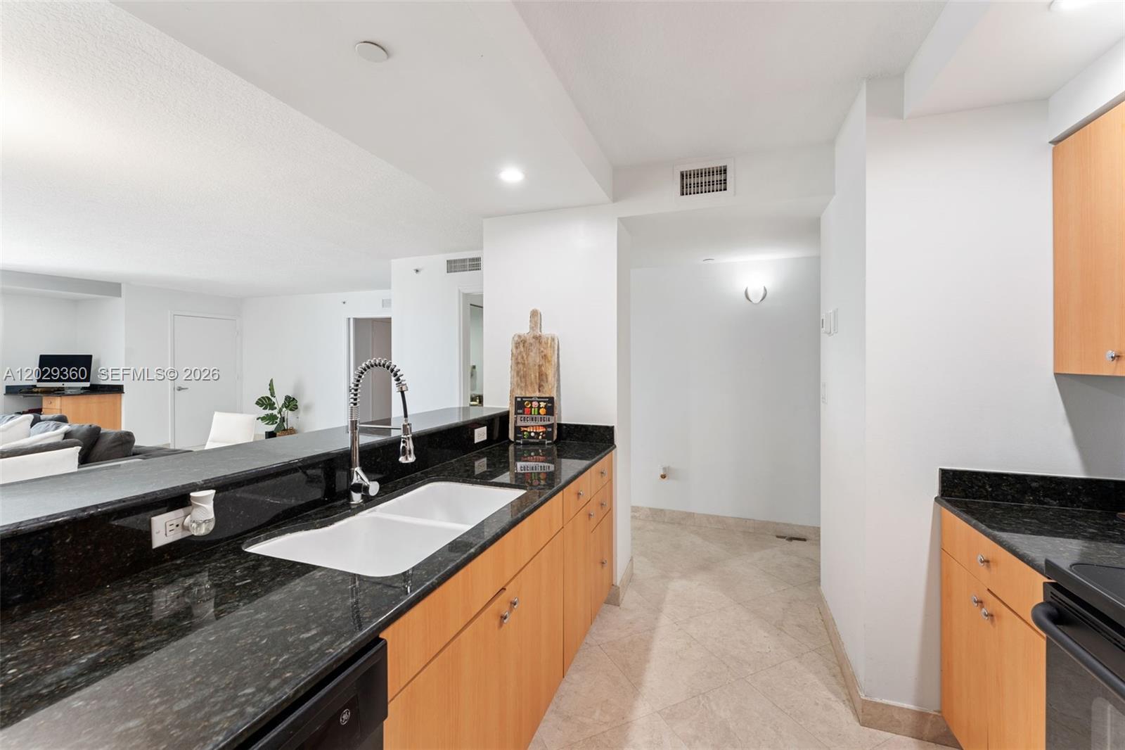 A kitchen features light wood cabinets, black granite countertops, and a white double-basin sink — 6917 Collins Ave # 607, Miami Beach FL 33141, MIAMI BEACH, FL