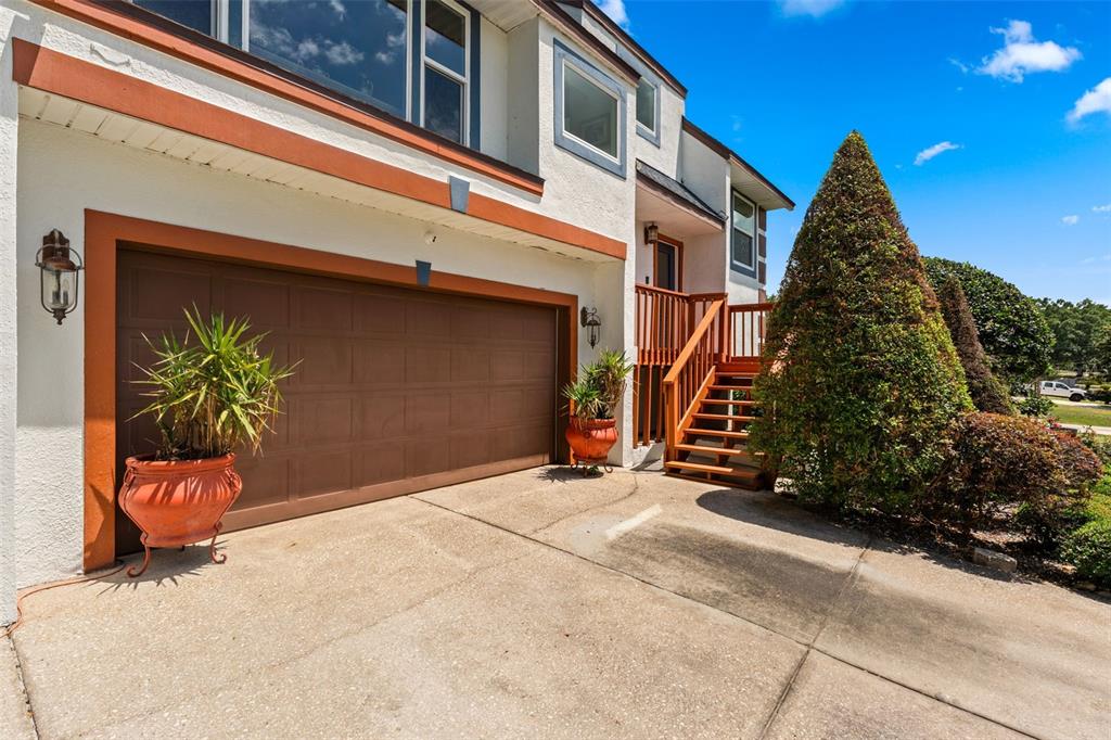 A two-story house exterior features a brown garage door, wooden stairs, and potted plants — 13332 SUBURBAN TERRACE, WINTER GARDEN, FL