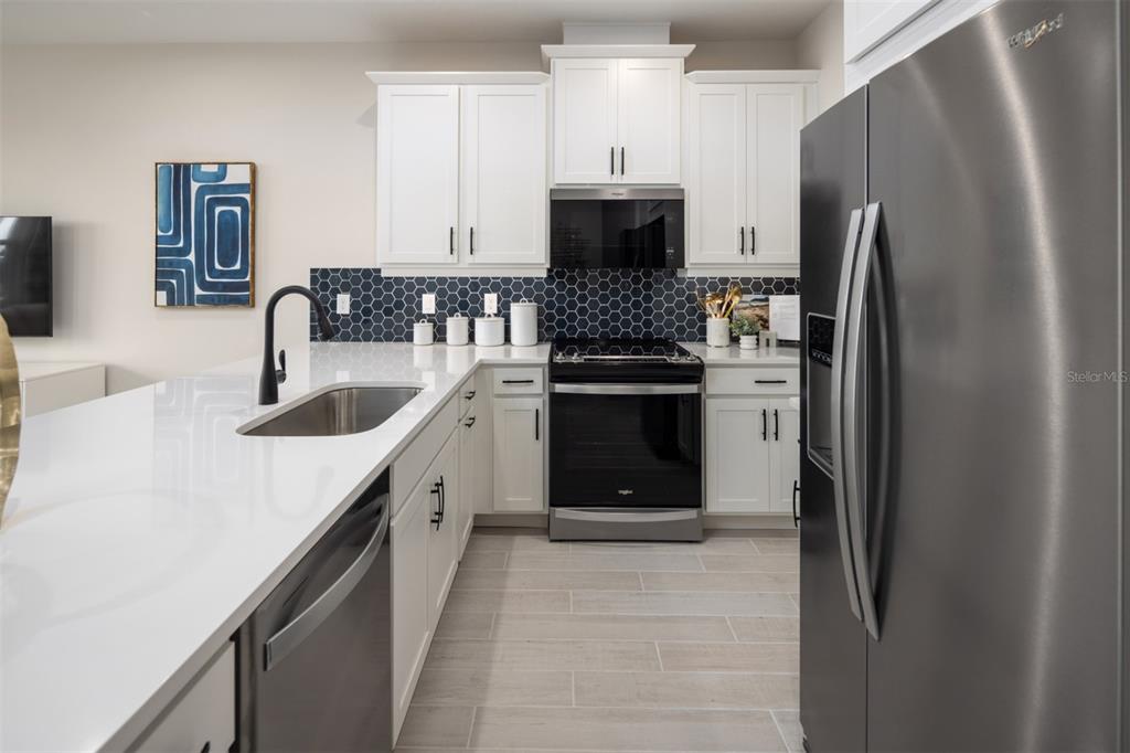 A modern kitchen features white cabinets, stainless steel appliances, and a dark blue hexagonal backsplash — 2812 CAMELLIA FLOWER STREET, APOPKA, FL