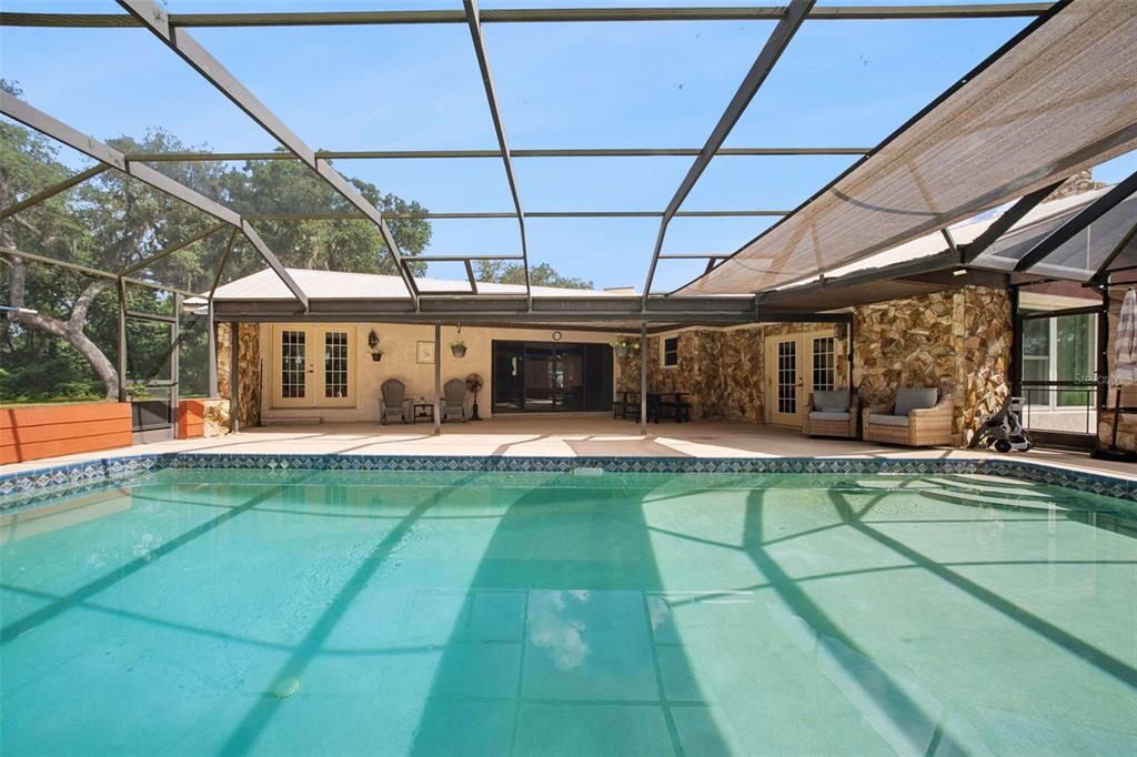 A swimming pool sits inside a screened-in lanai with a stone-accented exterior wall — 7232 E TURNER CAMP ROAD, INVERNESS, FL