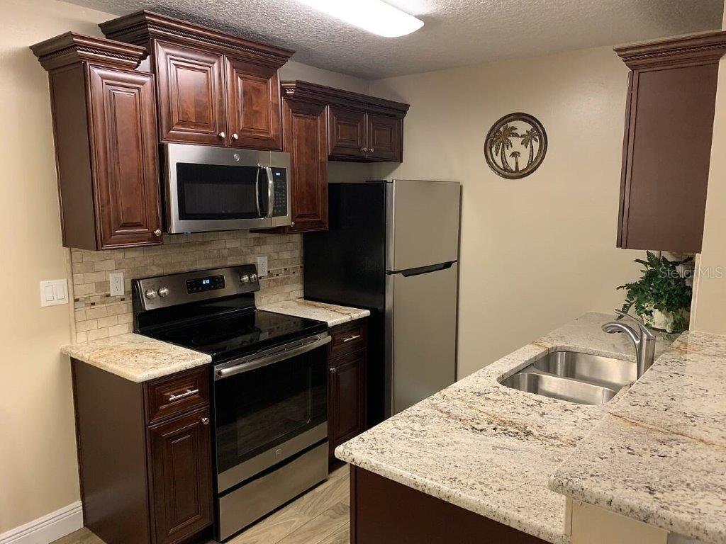 A kitchen features dark wood cabinets, stainless steel appliances, and light granite countertops — 2612 GRASSY POINT DRIVE UNIT 102, LAKE MARY, FL