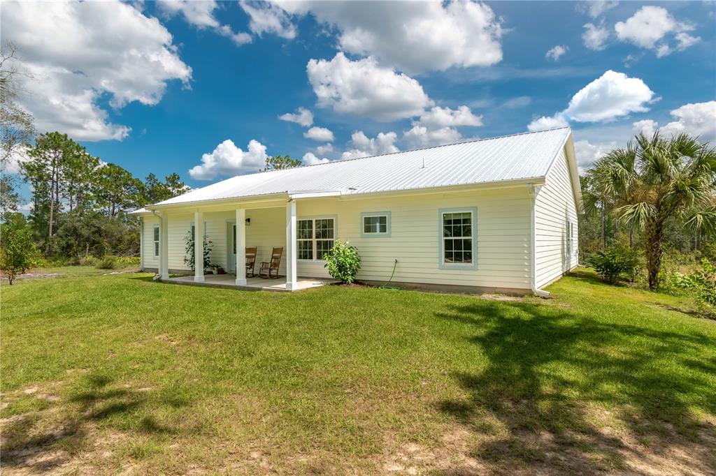 A light-colored house with a metal roof and a covered porch sits on a lawn — 14042 NE 110TH STREET, FORT MC COY, FL