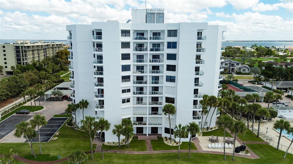 An aerial view of a white, multi-story residential building surrounded by palm trees and landscaping — 1050 LONGBOAT CLUB ROAD UNIT 506, LONGBOAT KEY, FL