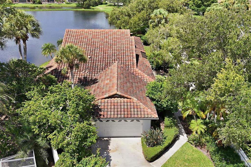 An aerial view of a house with a tiled roof, garage, and surrounding trees near water — 4300 CAMINO MADERA, SARASOTA, FL