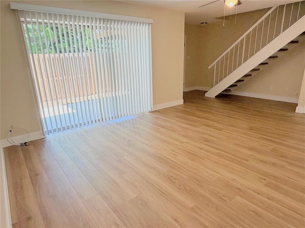 An empty living room features light wood-look flooring, vertical blinds on a sliding door, and stairs — 3205 DEER COURT, BRANDON, FL
