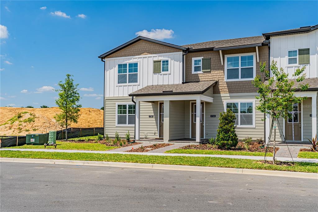 A two-story townhouse exterior with light siding, a covered entryway, and a grassy front lawn — 17344 SWEET MORO DRIVE, WINTER GARDEN, FL
