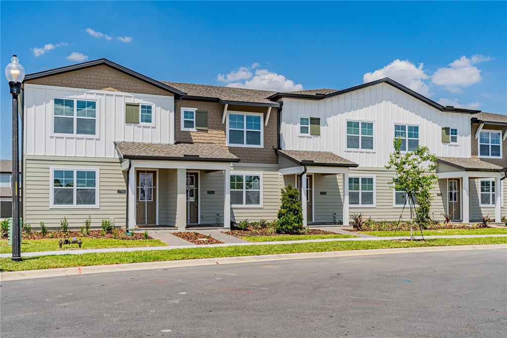 A row of two-story townhomes with light green siding, white vertical paneling, and brown shingled roofs — 17344 SWEET MORO DRIVE, WINTER GARDEN, FL