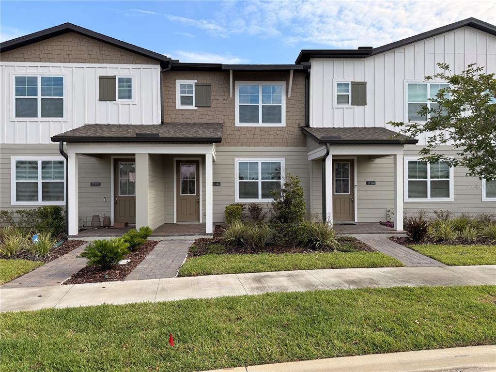 A row of three two-story townhomes with tan siding, white vertical accents, and covered entryways — 17344 SWEET MORO DRIVE, WINTER GARDEN, FL