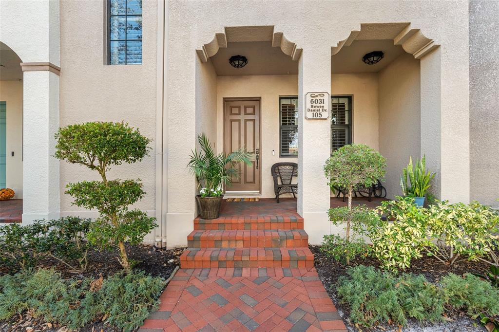 A brick walkway leads to the front entrance of a beige stucco home with arched porches — 6031 BOWEN DANIEL DRIVE UNIT 105, TAMPA, FL