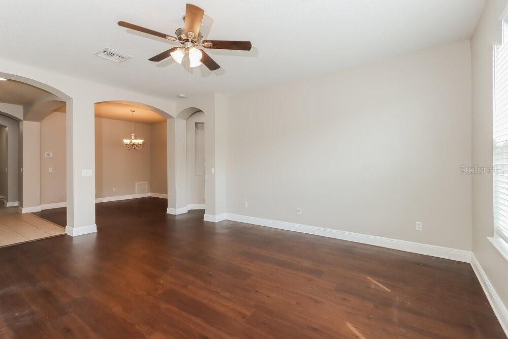 An empty living room features dark wood-look flooring, beige walls, and a ceiling fan — 7935 CAMDEN WOODS DRIVE, TAMPA, FL
