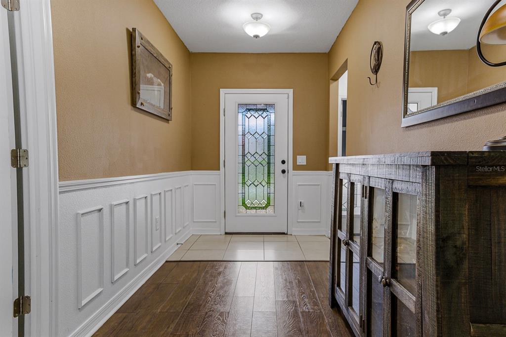 An entryway features wood-look flooring, white wainscoting, tan walls, and a glass-paneled front door — 18738 ALFARO LOOP, SPRING HILL, FL