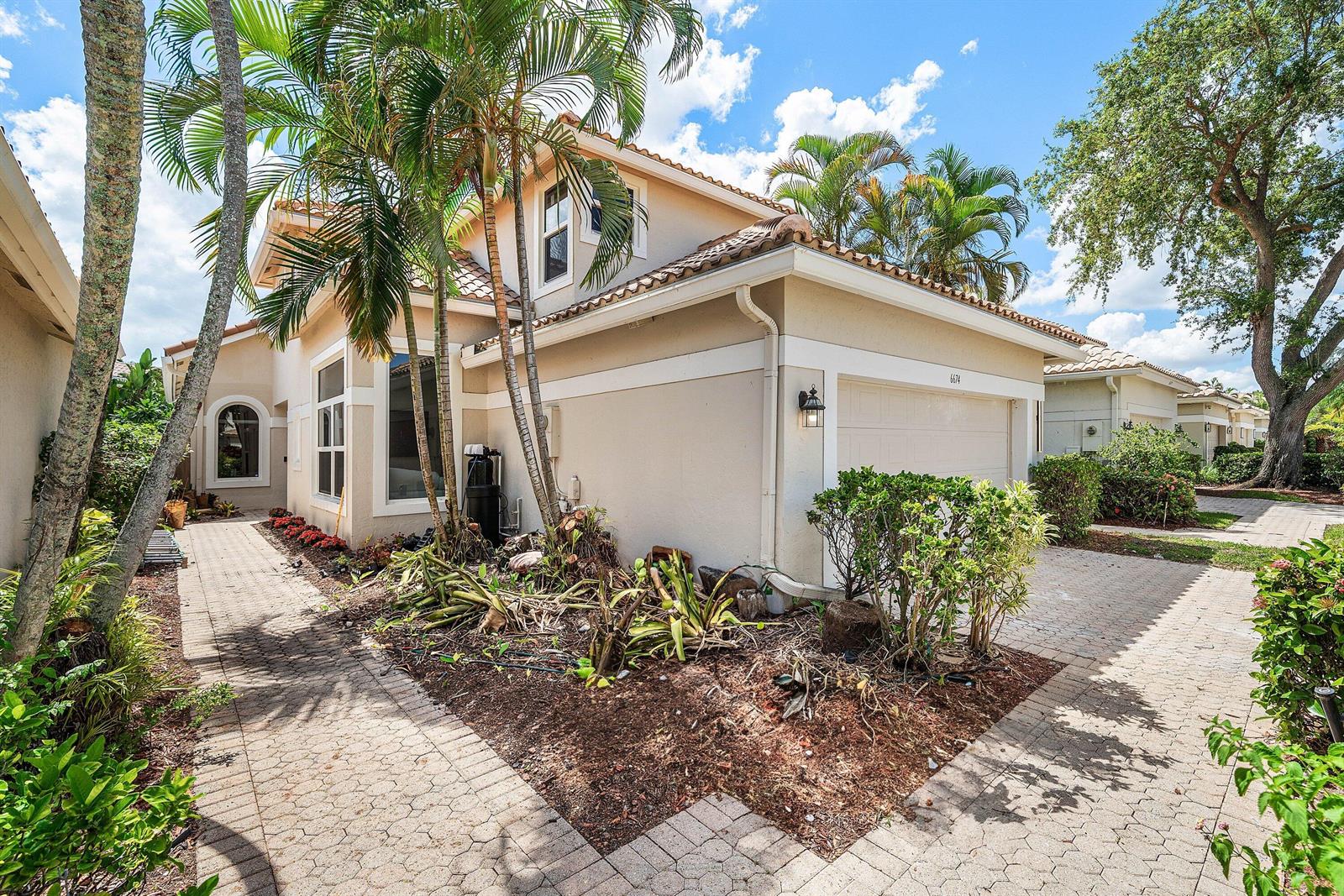 A two-story beige house features a paved walkway, a garage, and palm trees in front — 6674 NW 25th Avenue, Boca Raton FL 33496, BOCA RATON, FL