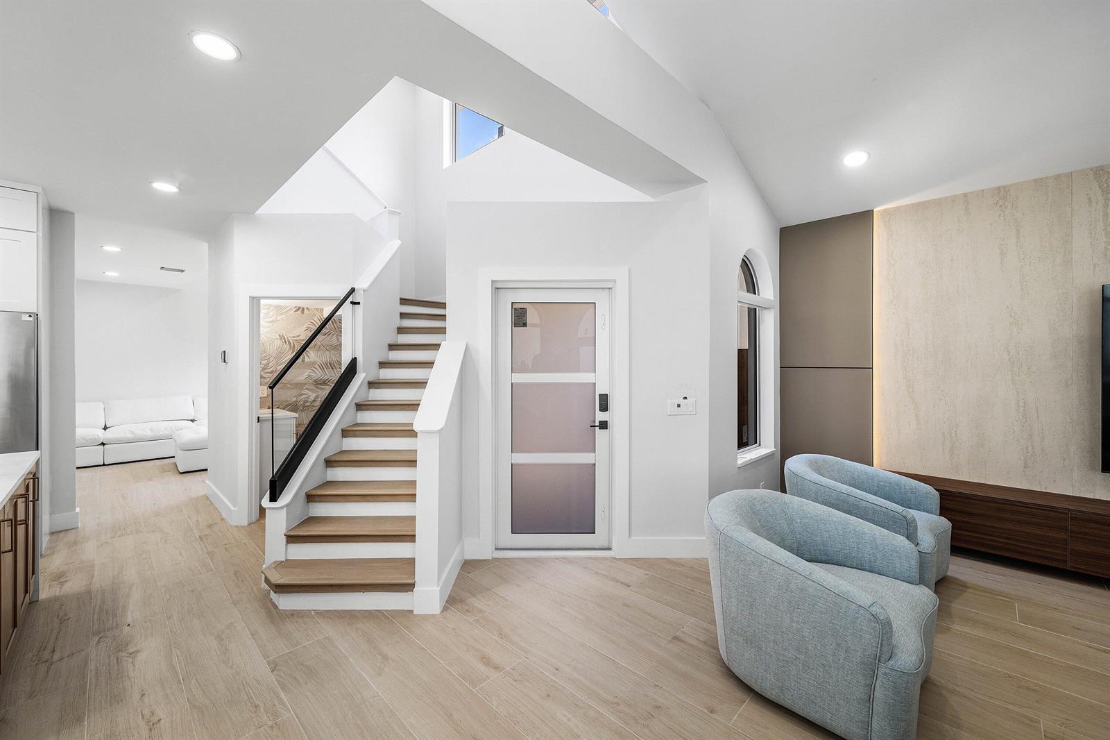 A modern living area features light wood floors, a staircase, and two light blue armchairs — 6674 NW 25th Avenue, Boca Raton FL 33496, BOCA RATON, FL
