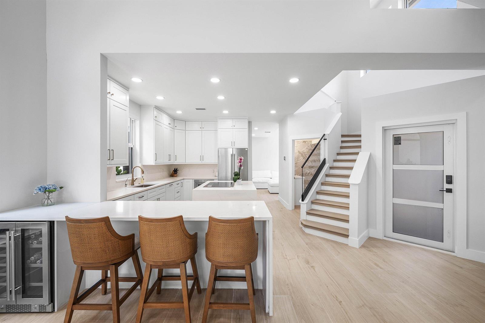 A modern kitchen features white cabinetry, a waterfall island, and a staircase with wooden treads — 6674 NW 25th Avenue, Boca Raton FL 33496, BOCA RATON, FL