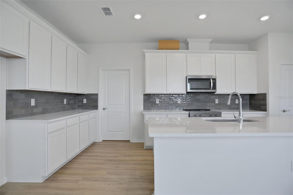 A modern kitchen features white cabinets, gray subway tile backsplash, and a large quartz island — 7839 GLEN LILY PLACE, PARRISH, FL