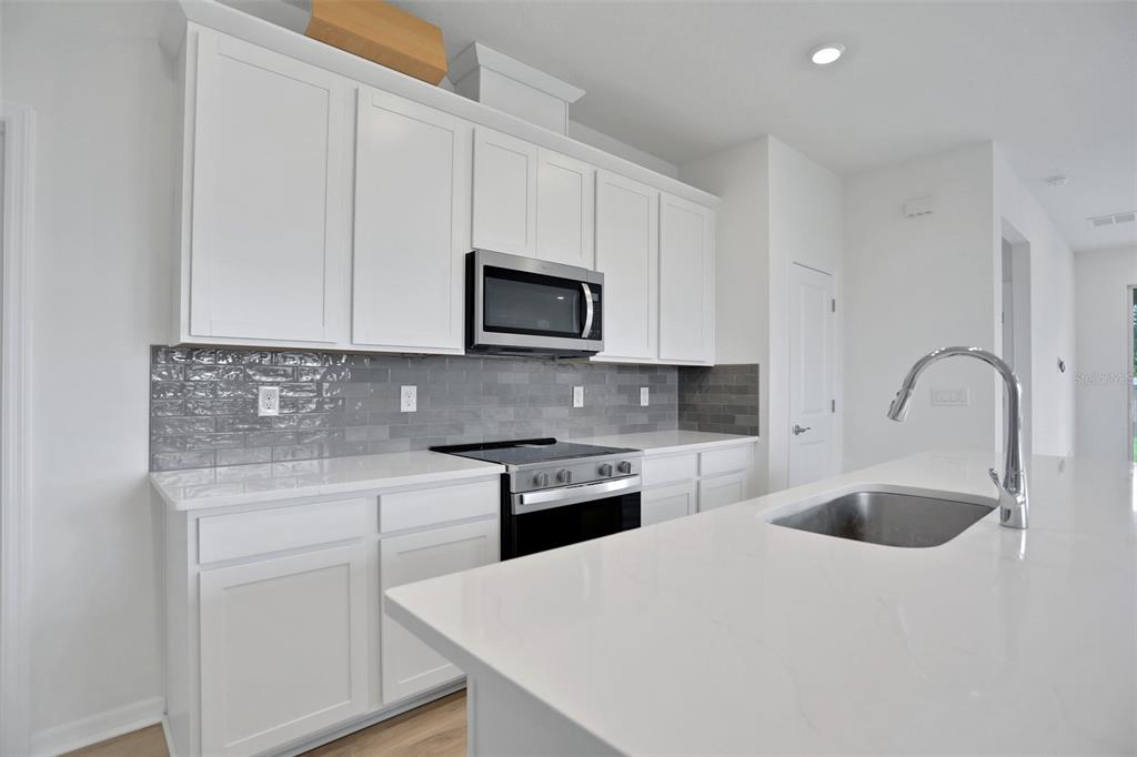 A modern kitchen features white cabinets, a gray subway tile backsplash, and a quartz island — 7839 GLEN LILY PLACE, PARRISH, FL