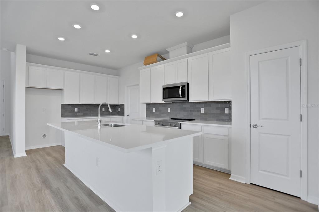 A modern kitchen features white cabinetry, a central island with a sink, and gray backsplash — 7839 GLEN LILY PLACE, PARRISH, FL