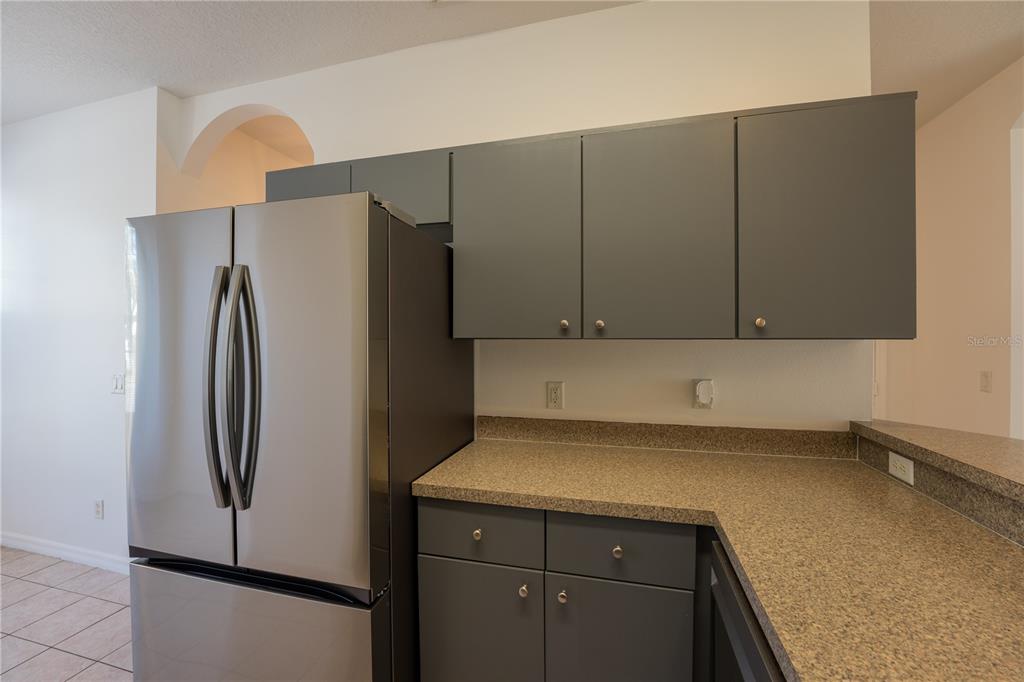 A kitchen features gray cabinets, a stainless steel refrigerator, and speckled laminate countertops — 4712 HEMINGWAY HOUSE STREET, KISSIMMEE, FL