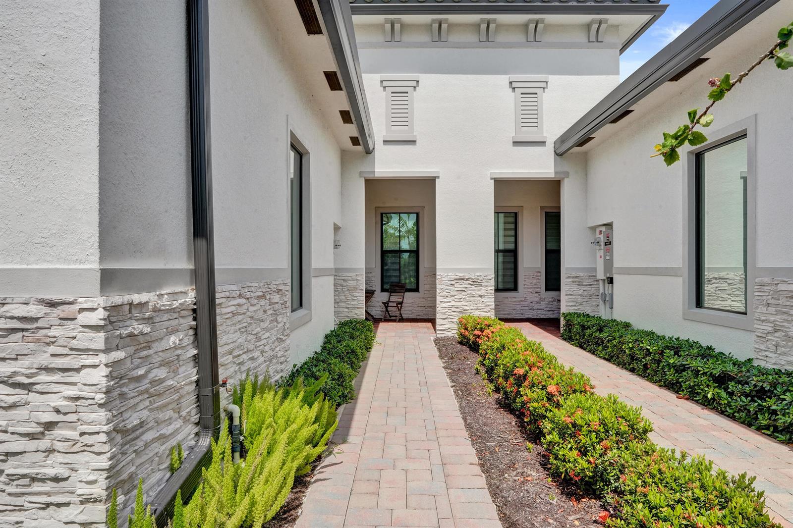A paved walkway leads between two white stucco buildings with stone accents and landscaped hedges — 8336 W Blue Spring Drive, Parkland FL 33067, PARKLAND, FL