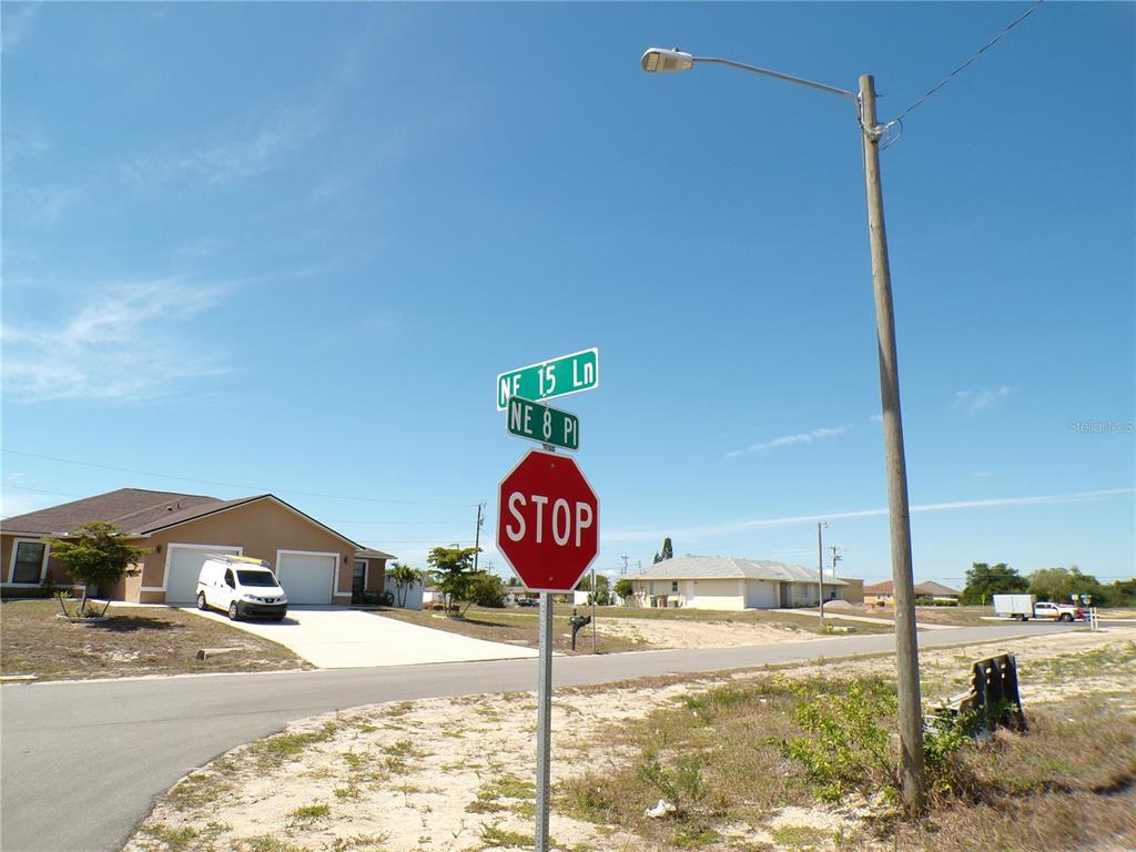 A stop sign and street name signs stand at a residential intersection under a blue sky — 821 NE 15TH LANE, CAPE CORAL, FL