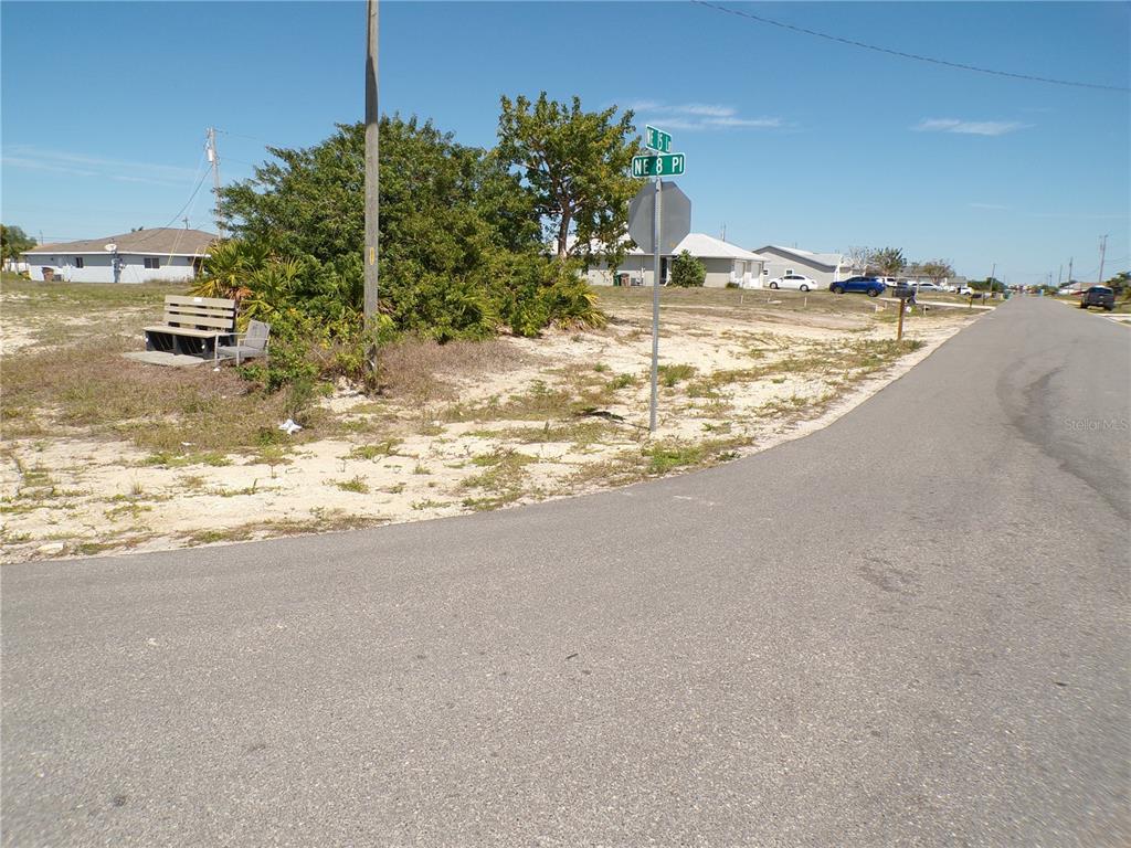 A street corner view shows a vacant sandy lot with a bench and street signs — 821 NE 15TH LANE, CAPE CORAL, FL