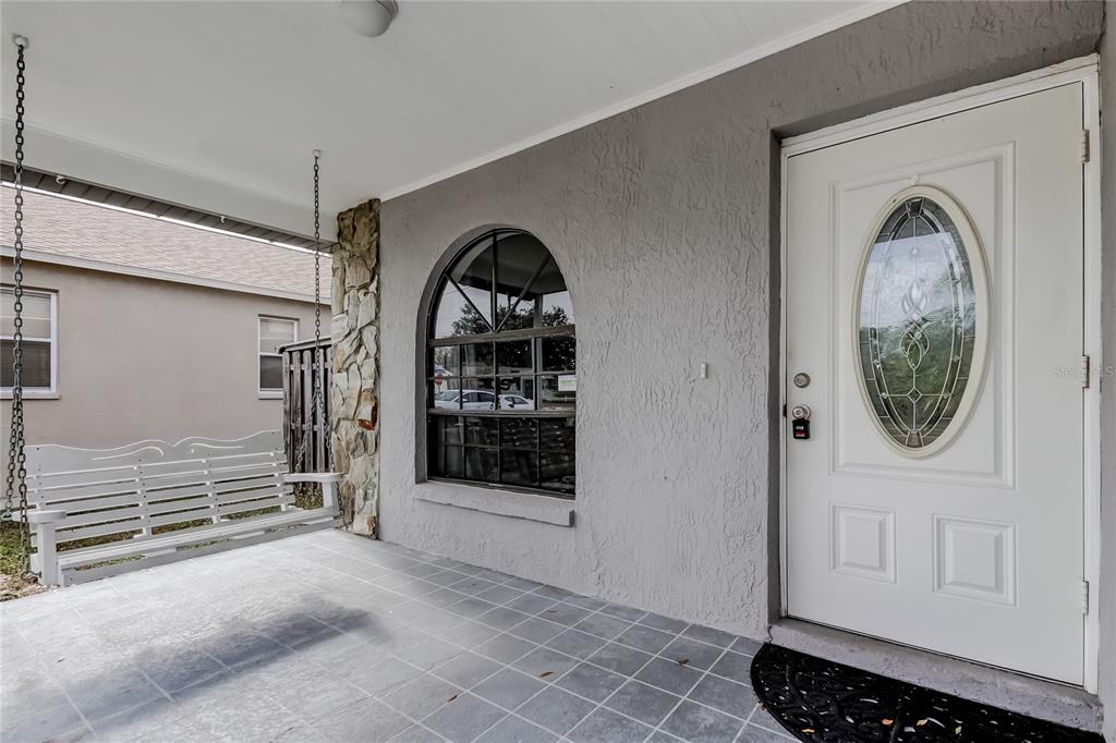 A covered front porch features a white swing, a gray stucco wall, and an arched window — 206 BEDFORD STREET, OLDSMAR, FL