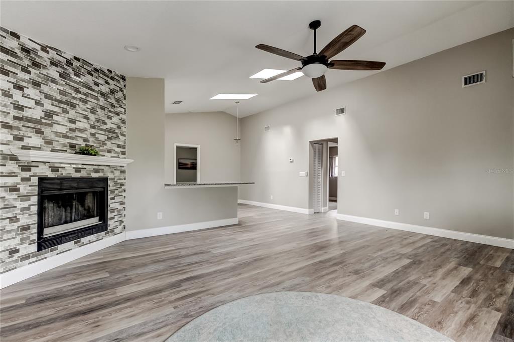 A living room with wood-look flooring, a stone fireplace, and a ceiling fan — 206 BEDFORD STREET, OLDSMAR, FL