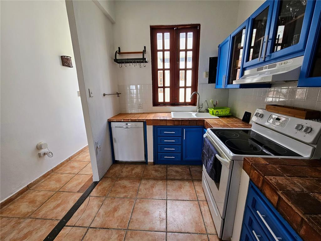 A kitchen features blue cabinets, tiled countertops, a white stove, and a window above the sink — 353 CALLE DE LA LUNA UNIT 301, OLD SAN JUAN, PR