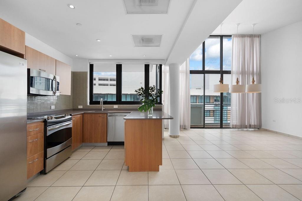A modern kitchen with wood cabinetry and stainless steel appliances opens to a bright living area — 1511 PONCE DE LEON AVENUE UNIT PH-481, SAN JUAN, PR