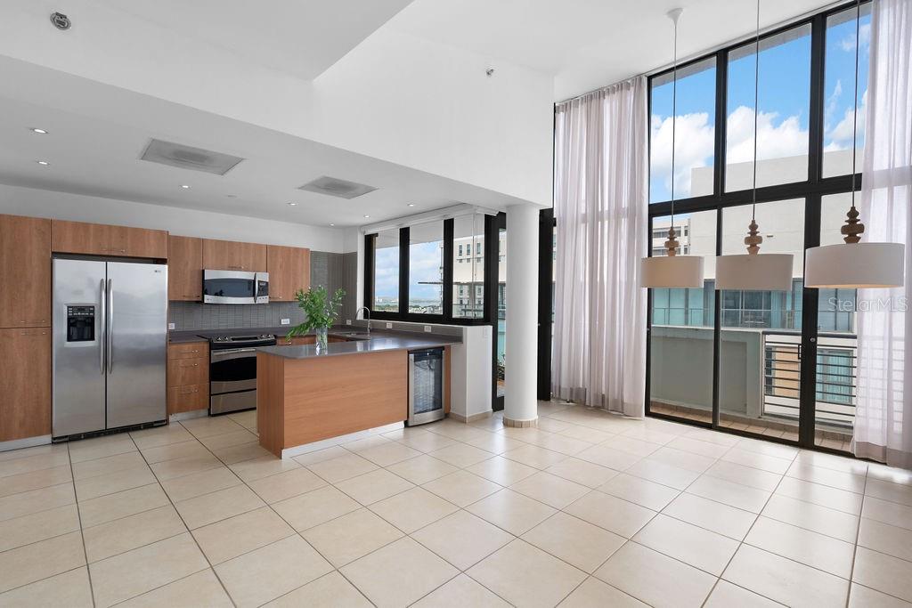 A modern kitchen with wood cabinets and stainless steel appliances opens to a bright living area — 1511 PONCE DE LEON AVENUE UNIT PH-481, SAN JUAN, PR