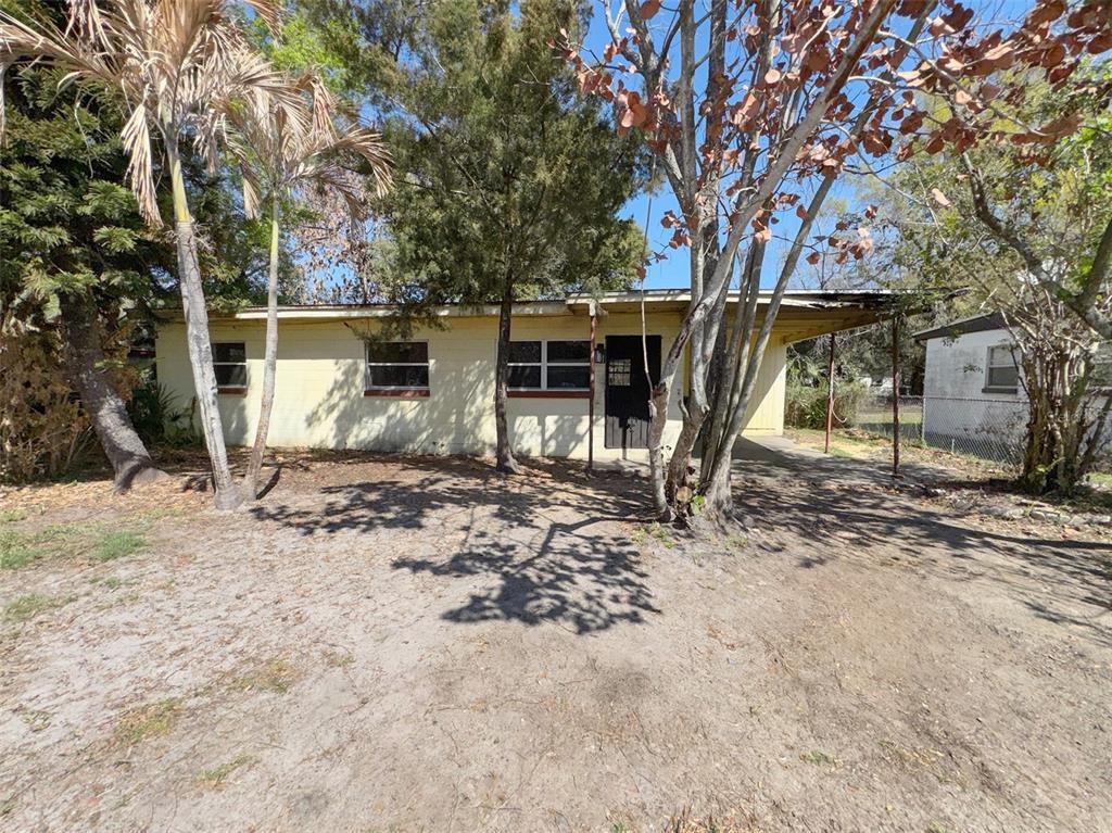 A single-story yellow house with a flat roof and a carport stands on a sandy lot — 2841 W AMELIA STREET, ORLANDO, FL