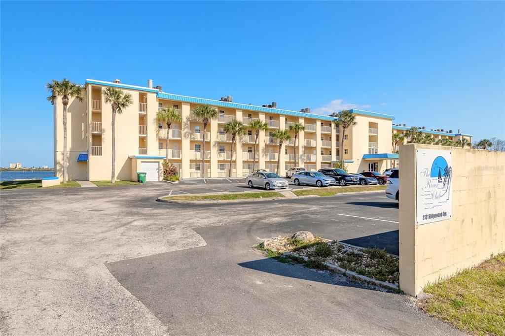 A multi-story apartment building with a parking lot and palm trees under a clear sky — 3131 S RIDGEWOOD AVENUE UNIT 101, SOUTH DAYTONA, FL