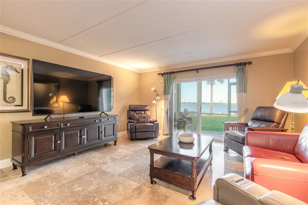 A living room with tile floors, a large television, and a sliding door overlooking water — 3131 S RIDGEWOOD AVENUE UNIT 101, SOUTH DAYTONA, FL