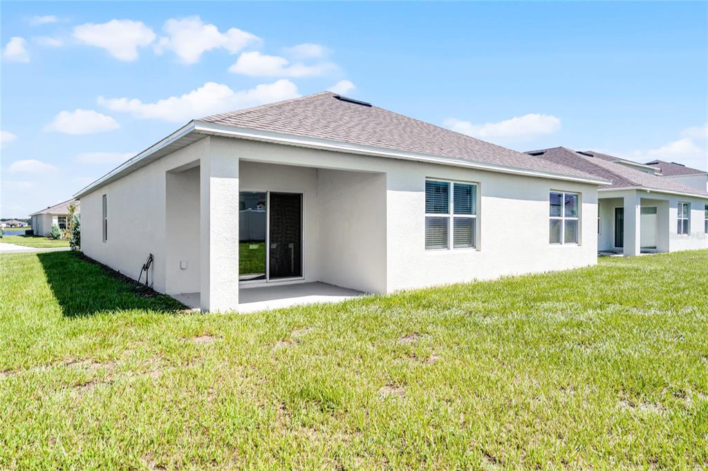 The exterior rear view of a single-story house features a covered patio and lawn — 1340 DAISY FIEL DR, WINTER HAVEN, FL