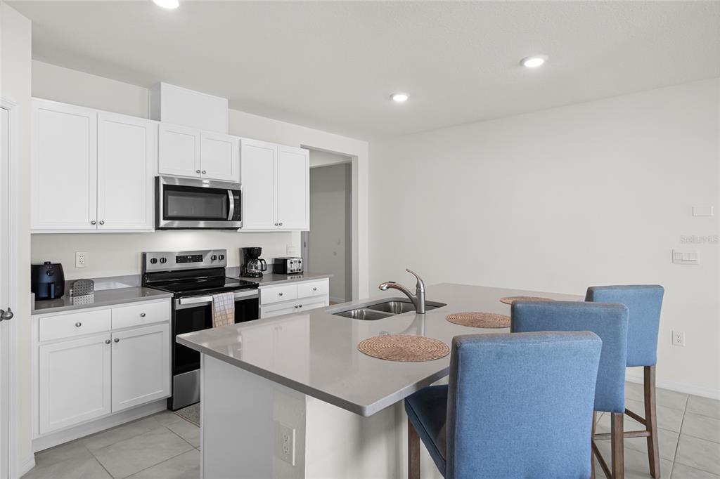 A kitchen features white cabinets, stainless steel appliances, a gray island, and blue bar stools — 1340 DAISY FIEL DR, WINTER HAVEN, FL