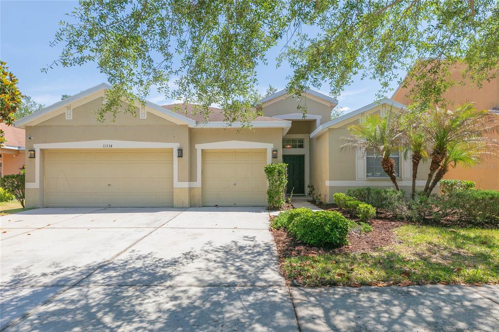 A single-story house with a two-car garage, beige stucco exterior, and a front entryway — 11334 BRIDGE PINE DRIVE, RIVERVIEW, FL