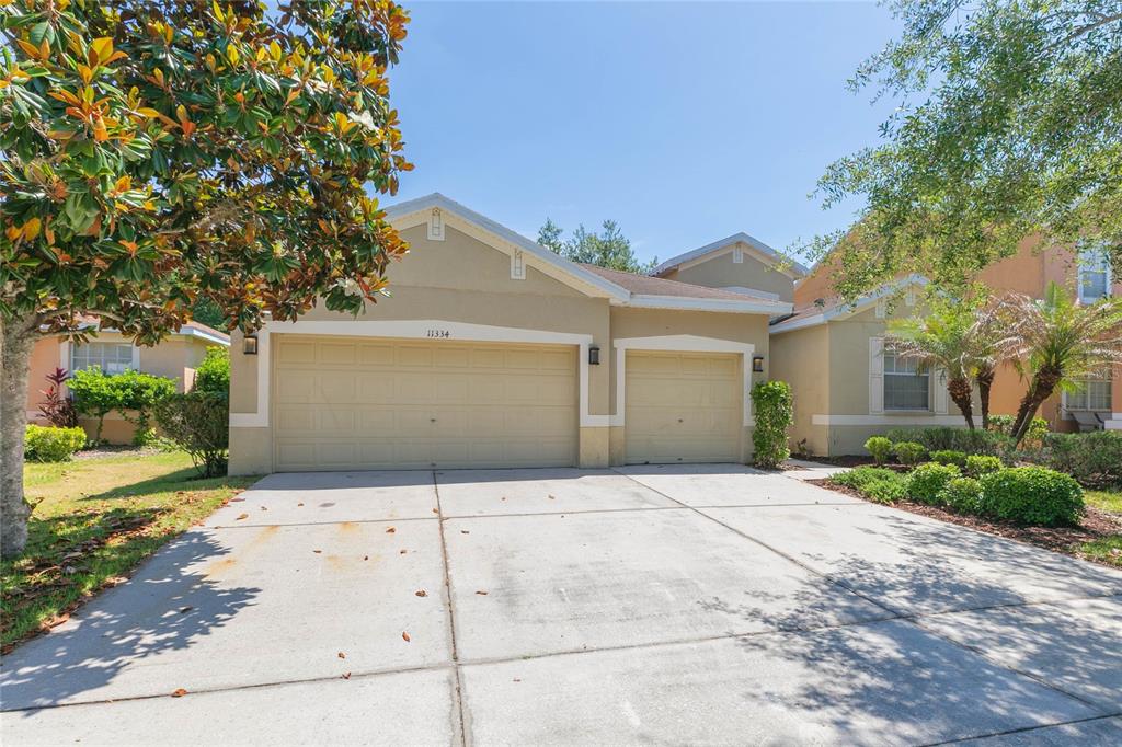 A beige single-story house features a three-car garage and a concrete driveway — 11334 BRIDGE PINE DRIVE, RIVERVIEW, FL