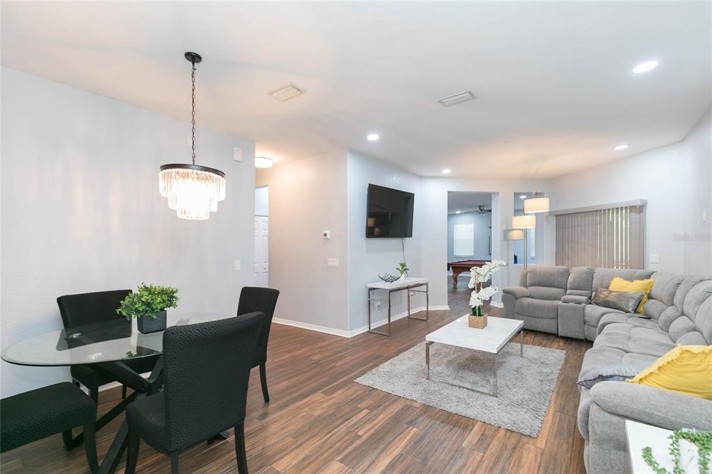 An open-concept living and dining area features wood-look flooring, a gray sectional, and a chandelier — 11334 BRIDGE PINE DRIVE, RIVERVIEW, FL