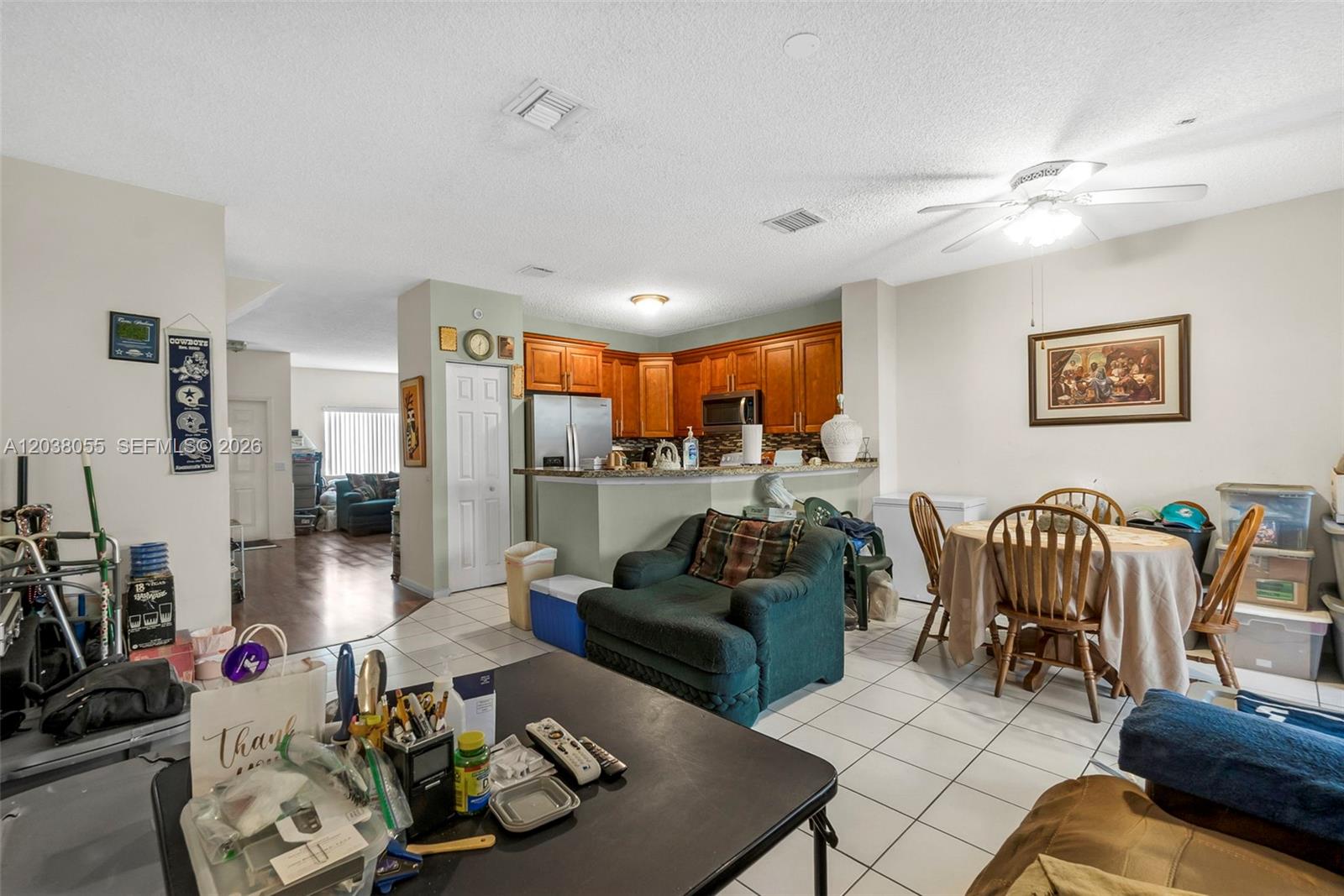A kitchen with wood cabinets and a breakfast bar overlooks a dining and living area — 783 NW 42nd Pl, Deerfield Beach FL 33064, DEERFIELD BEACH, FL