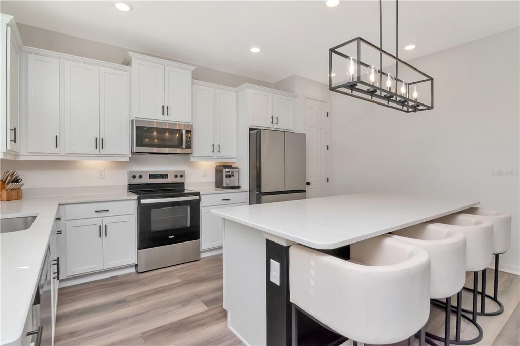 A modern kitchen features white cabinets, stainless steel appliances, and a large central island — 6384 BURNING OPAL BEND, LAND O LAKES, FL