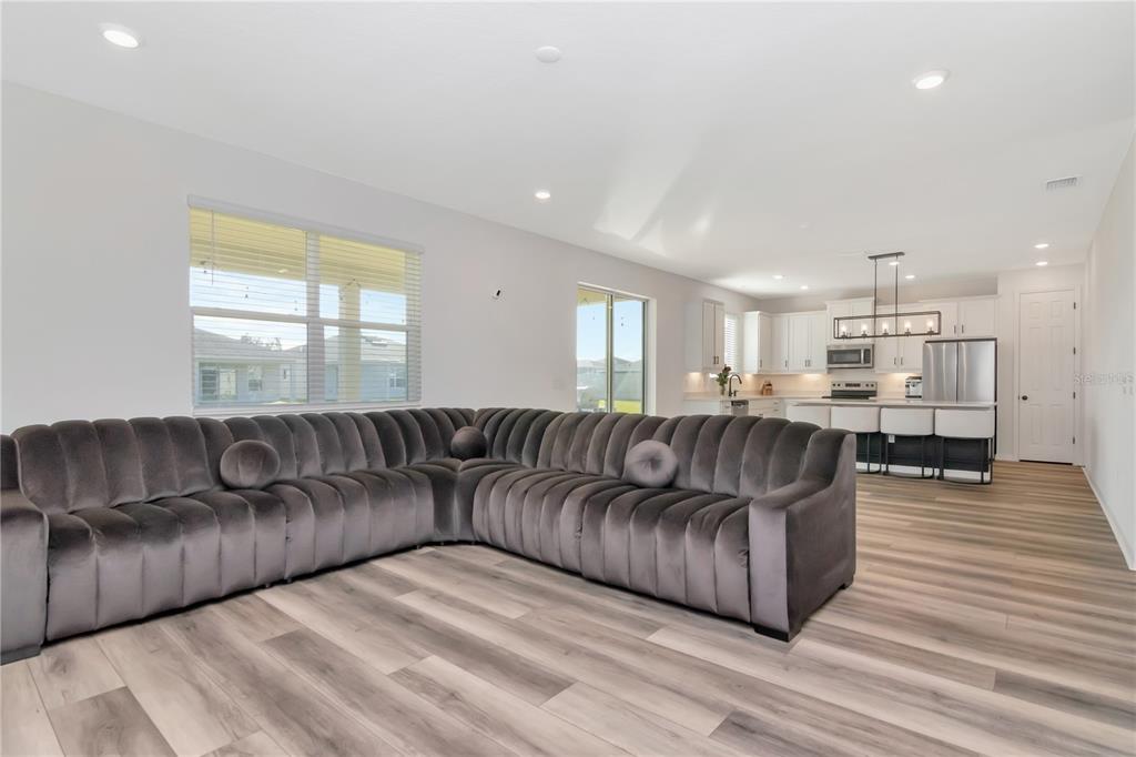 A spacious open-concept living room features a large grey velvet sectional and wood-look flooring — 6384 BURNING OPAL BEND, LAND O LAKES, FL