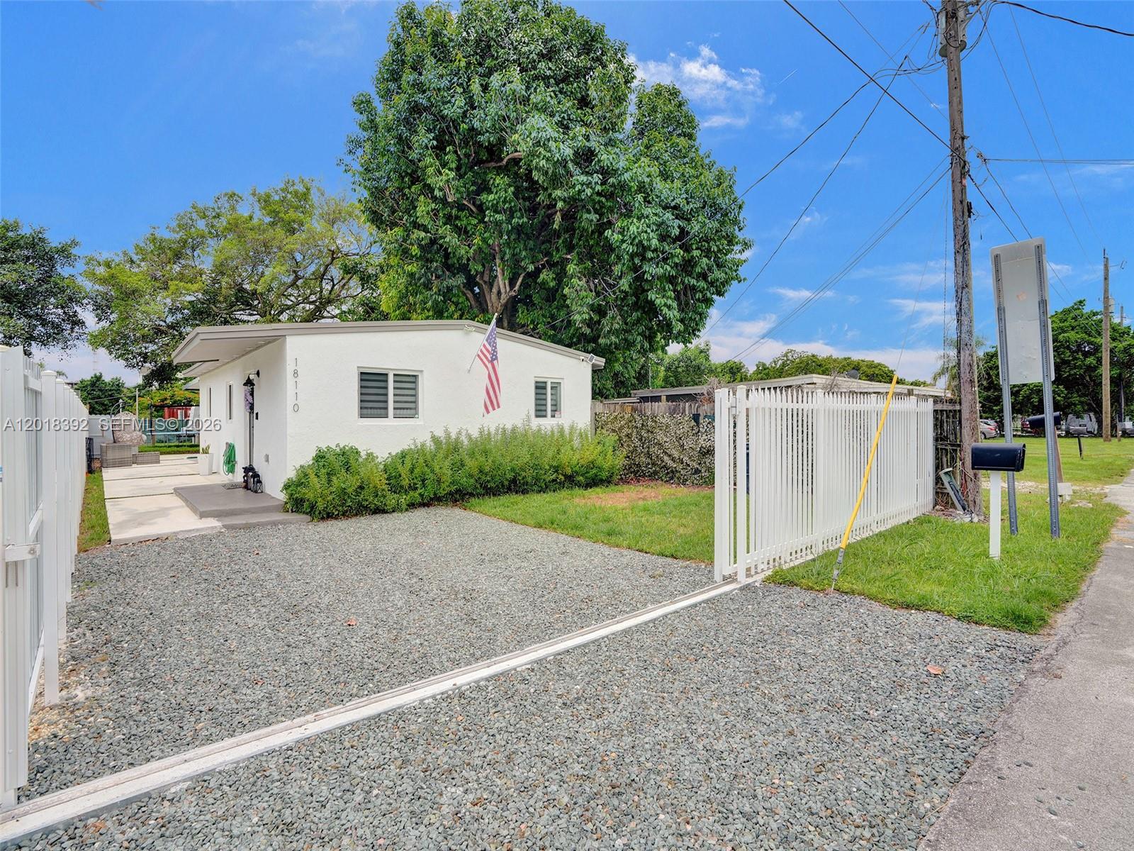 A white house with a gravel driveway and a white picket fence under a blue sky — 10222 SW 181st St, Miami FL 33157, MIAMI, FL